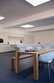 Minimalist wooden table and white shell chair in open-plan interior with kitchen counter