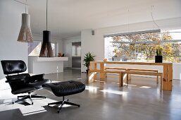 Klassiker Sessel mit schwarzem Lederbezug und passendem Fussschemel vor moderner Esstischgarnitur aus Holz in offenem Wohnraum