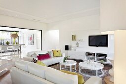 Sofalandschaft mit farbigen Kissen und Beistelltischen vor Medienregal im offenen, weiss gestalteten Wohnraum