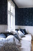 Blue and white patterned scatter cushions and seat cushions on bench below window and blue patterned wallpaper