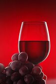A glass of red wine and some red grapes against a red background