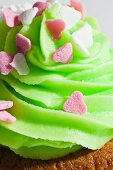 A cupcake topped with green icing and small sugar hearts (close-up)