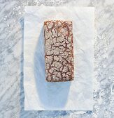 A wholemeal sandwich loaf on paper, on a marble slab, dusted with flour