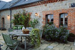 Seating area with faded garden furniture in front of climber-covered stone facade of French country manor