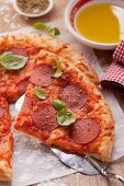 Pizza with salami and basil; one slice of the pizza is on a pizza shovel