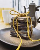 A yellow cord tied around pieces of chocolate, on a ceramic dish in front of a vintage coffee pot