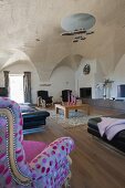 Black leather sofa and reading chair with patterned upholstery in spacious living room with designer lamp hanging from vaulted ceiling