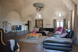 Black leather couch and matching ottoman in spacious living room with vaulted ceiling and designer pendant lamp