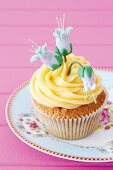 Cupcake mit gelbem Frosting und blauen Zuckerblüten