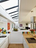 Designer kitchen with colourful wall tiles below skylight in modern, open-plan interior