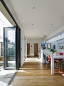 Dining table and colourful chairs on wooden floor in open-plan interior with folding glass door