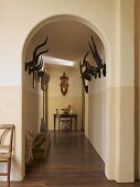 View through historic arched doorway along corridor with row of antlers on wall