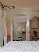 Bed with white bedspread and voile draped from canopy frame; bathroom in background