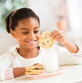 A girl dunking a biscuit in a glass of milk