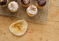 Cupcakes auf einem Abkühlgitter; daneben eine leergegessene Papiermanschette