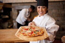 Pizzabäckerin zeigt Pizza auf Holzschaufel