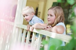 Bruder und Schwester blicken über das Geländer einer Veranda