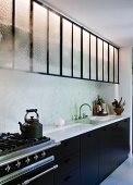 Kitchen counter with marble worksurface, black base units and wall cabinets with glass doors