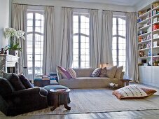Sessel mit Fusshocker und Sofa vor raumhohen Sprossenfenster mit hellgrauen Vorhängen im Jugendstil Wohnzimmer