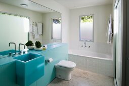 Designer bathroom with full mirror wall above a bright blue vanity with a trough sink