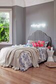 Bed with grey curved headboard, subdued blue and white bed linen and bright scatter cushions