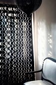 Dark wooden chair with white upholstery next to curtain with white wavy pattern on dark fabric