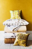 Folded, elegant quilts, bed linen and scatter cushions against golden yellow wall