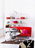 Black and white bed linen on red futon sofa bed in front of colour-coordinated decor on open shelving