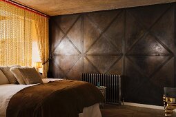 Double bed next to brass-coloured chain curtain and dark, wood-panelled wall in masculine bedroom