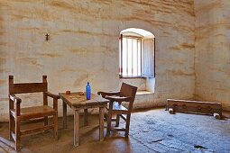 Holztisch mit Stühlen und eine umgefallene Bank in einem Raum mit Lehmziegelwänden, Mission La Purisima State Historic Park, Lompoc, Kalifornien