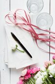 Ranunkelblüten, weiße Papiertüten, Stift, Geschenkband und Gläser auf weißem Holzuntergrund