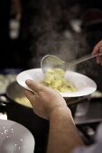 A chef spooning fresh tortellini onto a plate