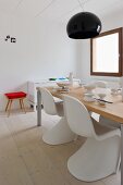 White plastic shell chairs at a modern dining table under a black, circular hanging light in a minimalist room