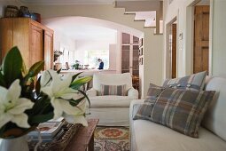Tartan scatter cushions on sofa next to armchair with view into kitchen through wide, arched open doorway