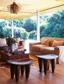 Seating area with sofa, African wooden stools & coffee table in interior with open sliding doors leading to garden