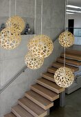 Pendant lamps with spherical, woven lampshades in foyer with floating staircase on exposed concrete wall