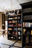 Dark, varnished, free-standing bookcases and white, metal chandelier on ceiling of open-plan living area