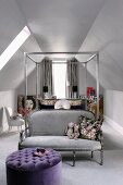 Metall-Himmelbett unter den Dachschrägen mit silbergrauer Couch am Fussende und davorstehendem violetten Polsterhocker