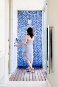 Shower in bright shower room with wooden board floor and mosaic-tiled wall