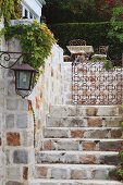 View up stone steps of wrought iron gate leading to terrace seating area and hedge in manorial setting