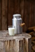 A milk churn and a milk glass on a rustic wooden block