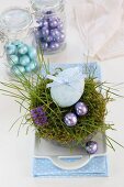 An egg decorated with a ribbon and chocolate eggs in an Easter nest made of moss and grass