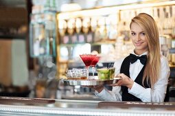 A waitress holding a tray of cocktails in a restaurant