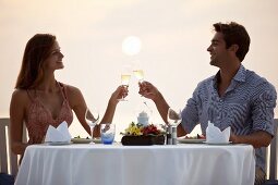 Paar stösst mit Sektgläsern an beim romantischen Dinner am Meer