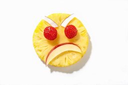 An angry face made from pineapple, apple, raspberries and coconut