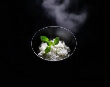 A Steaming Bowl of Japanese Rice with a Small Shiso Leaf; Black Background