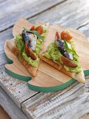 Bread triangles topped with avocado purée, tomatoes and sardines