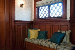 Kissen auf eingebaute Holzbank an holzvertäfelter Wand unter dem Fenster