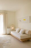 Moderne Malerei über einfacher Sofakonstruktion mit dicker Matratze und Polsterrolle in minimalistischem Wohnraum