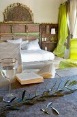 Olive twig and glass on table in front of double bed with white bed linen in simple bedroom